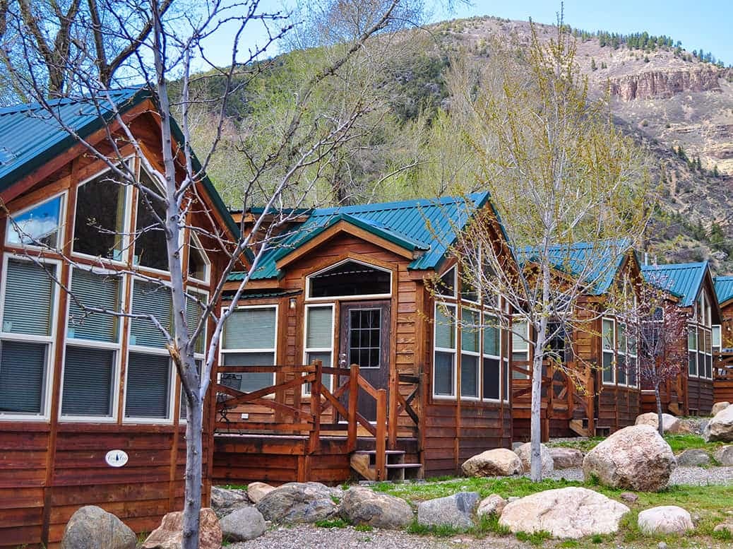Colorado RV Resort featuring a row of cabins nestled in a wooded area, with scenic mountains in the background.