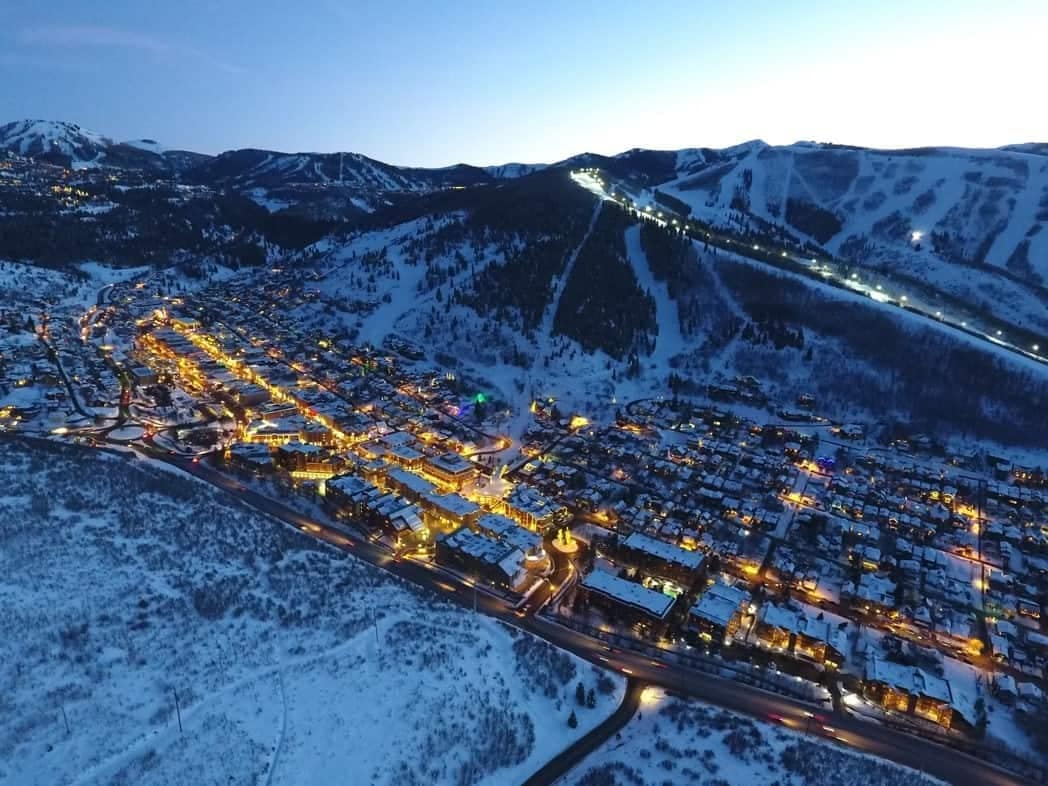 An aerial view of a ski town at night, featuring glamping units nestled among the snow-covered mountains.