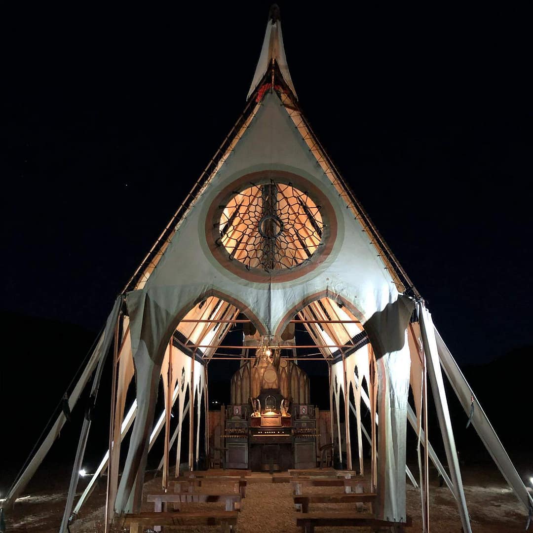 A large tent, inspired by the arts of Colorado, is beautifully lit up in the desert at night, creating a mesmerizing glamping experience.