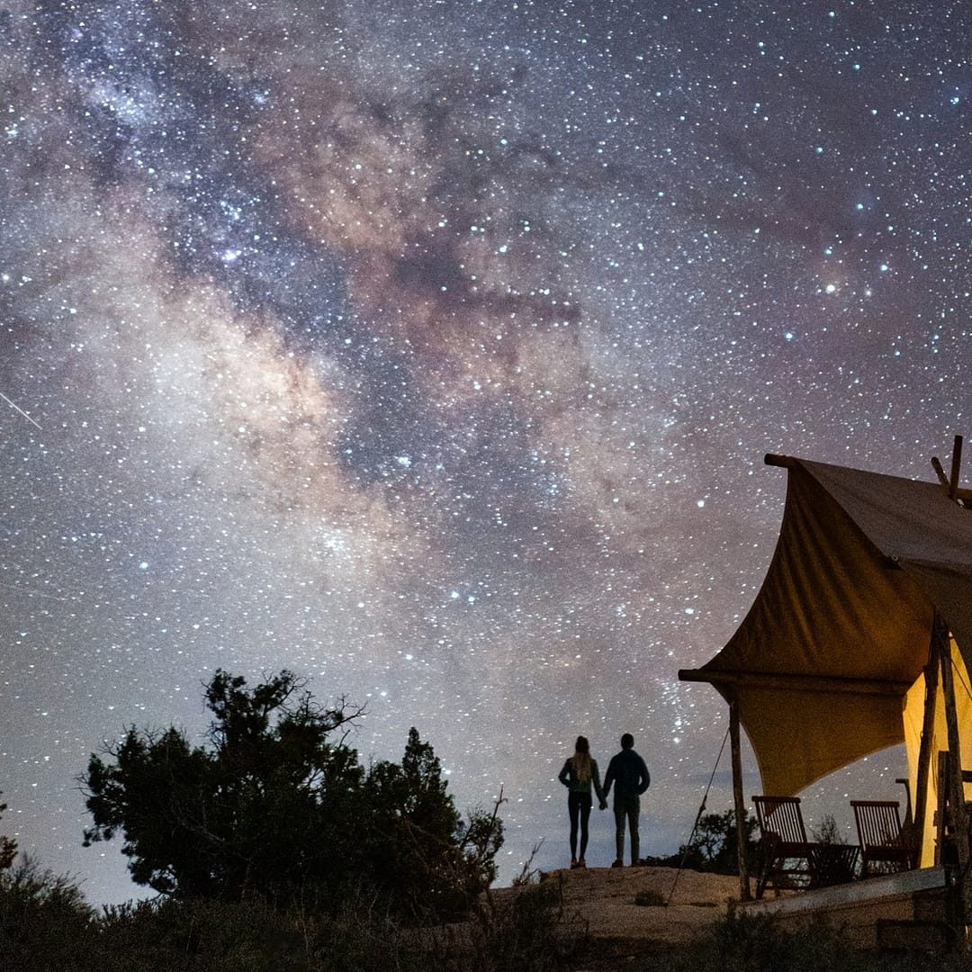Two people standing in front of a Safari-Inspired tent under the milky way.