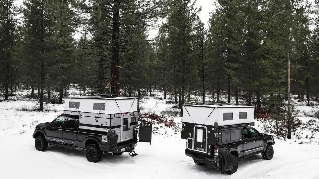 Two Four Wheel Campers parked in the snow next to each other.