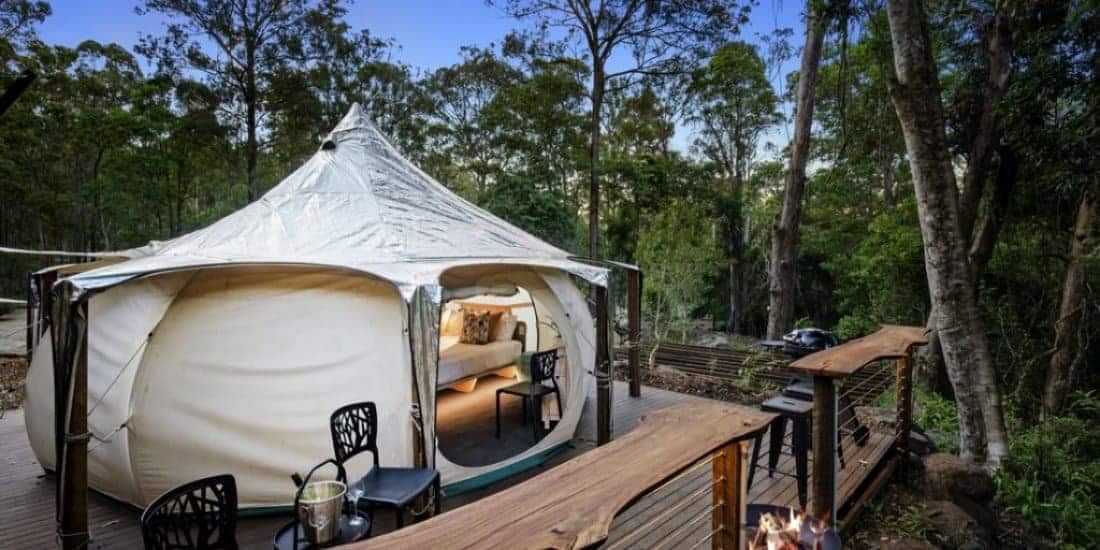 An Australian glamping site features a white tent situated on a wooden deck amidst the peaceful woods.