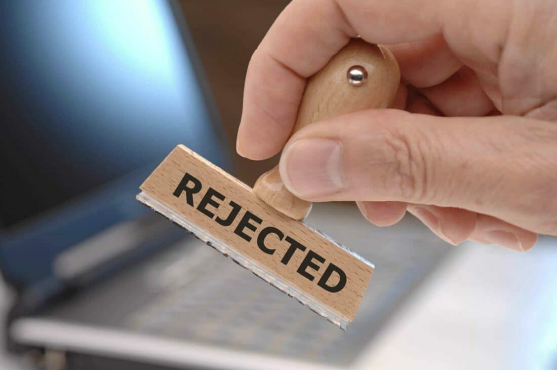 A person holding a wooden stamp with the word rejected in front of a laptop during development.