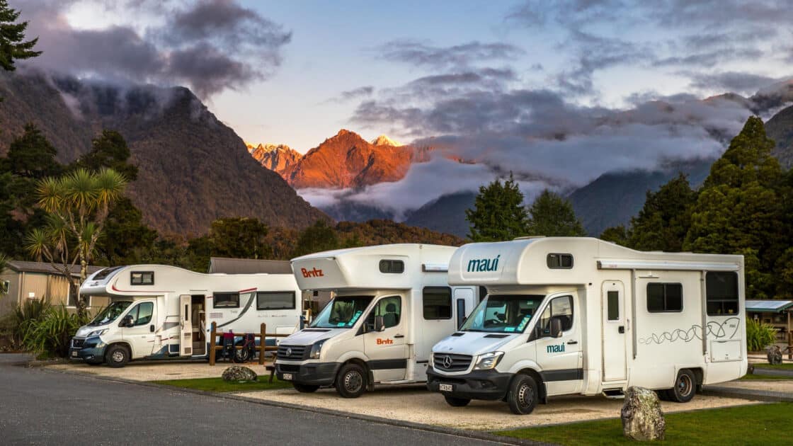 Three rvs parked in front of Glacier Country mountains.