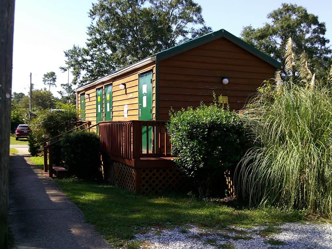 A small green Milton cabin with bushes in front of it.