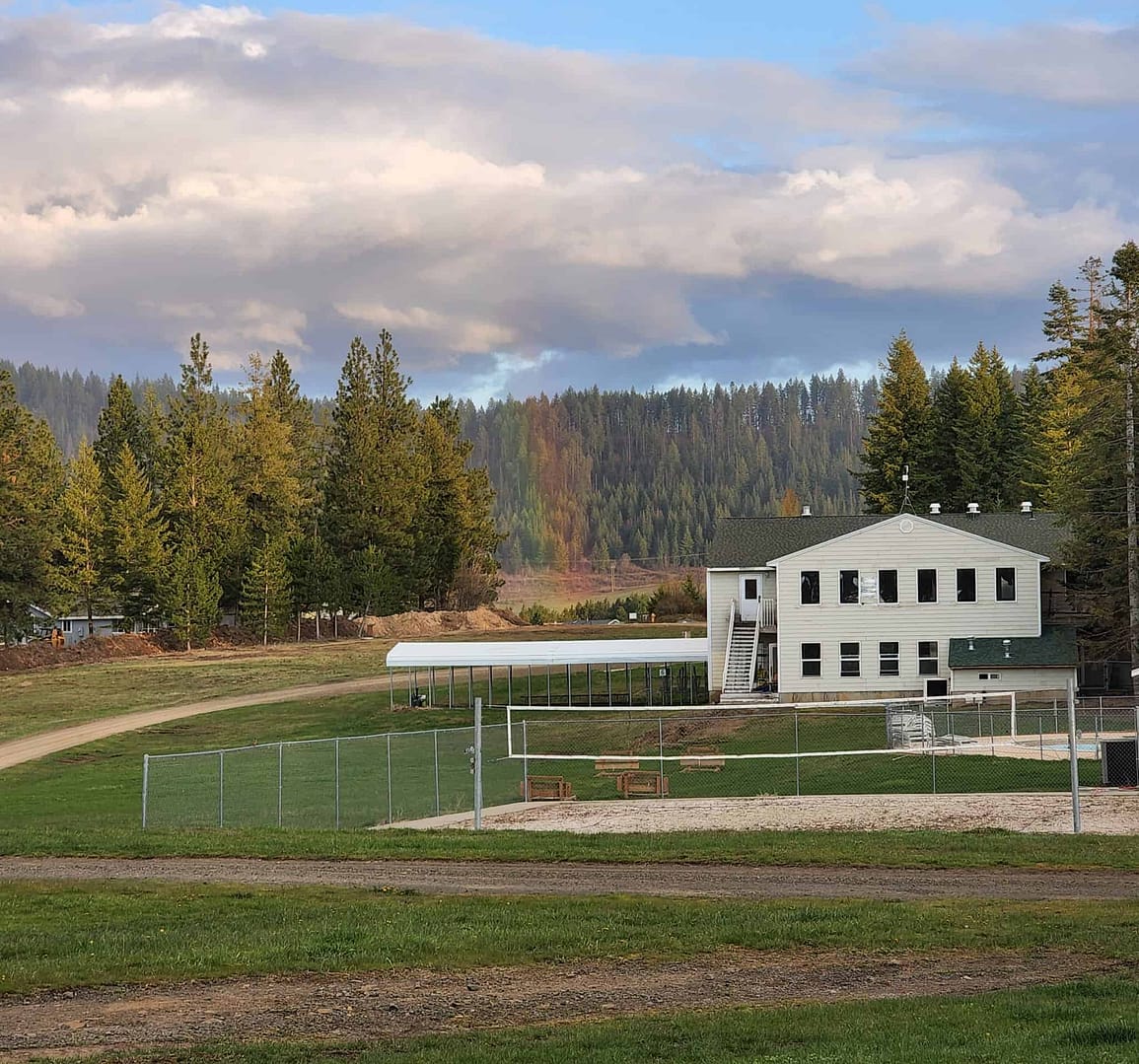 A former Nudist Retreat transformed into an RV Resort, featuring a white building against the backdrop of a vibrant rainbow in the sky.