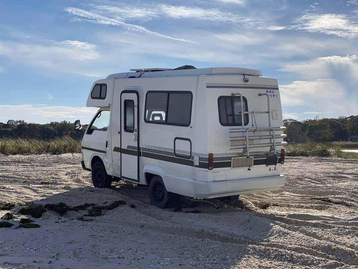 An Antique Japanese Camper, the Isuzu Fargo Alamo, parked on a sandy beach.