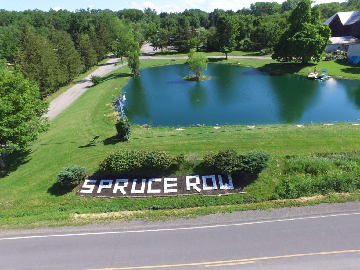 The sign for the Spruce Row Campground is in front of a pond.