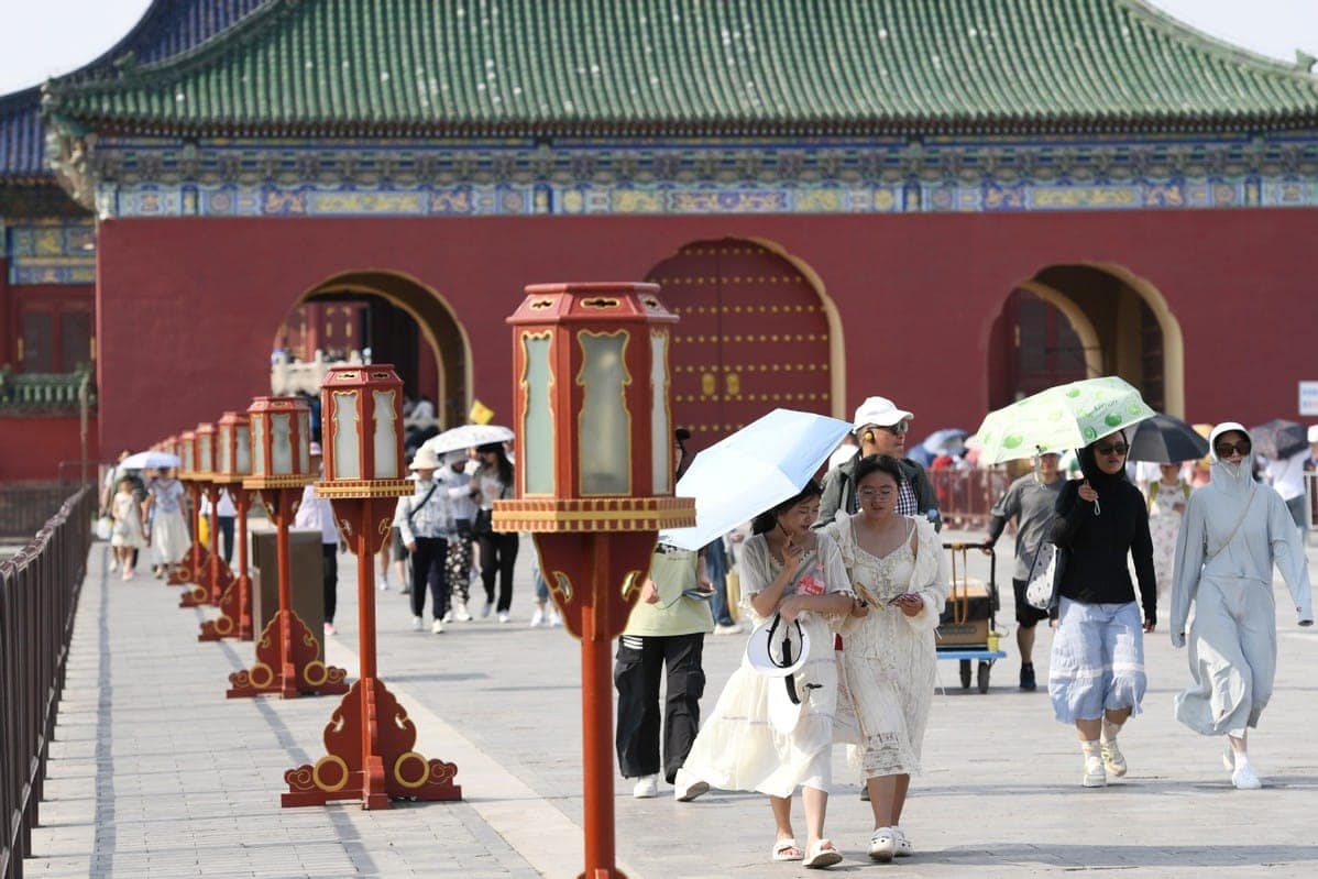 A group of people enjoying tourism during Dragon Boat Holiday, strolling through the forbidden city with umbrellas.