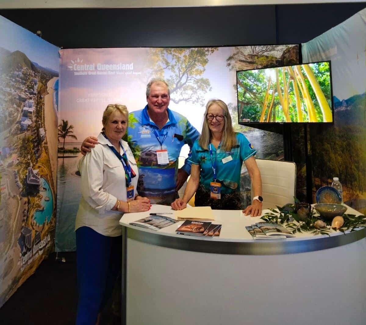 Three people posing in front of a display booth at the Caravan and Camping Super Show.