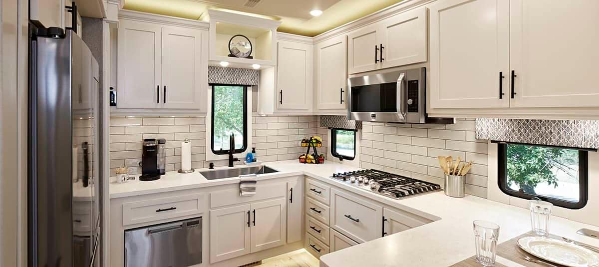 A kitchen showcasing white cabinets and stainless steel appliances, featured at the New Horizons RV Showcasing.