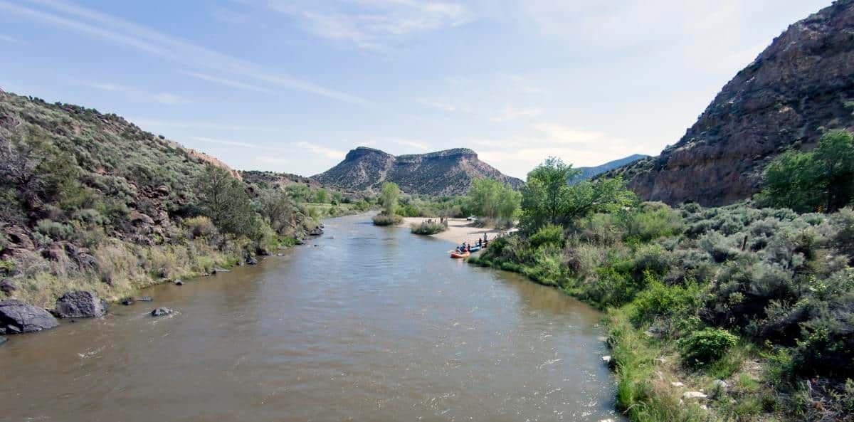 An outdoor startup nestled in the mountains of New Mexico, surrounded by a river and trees.