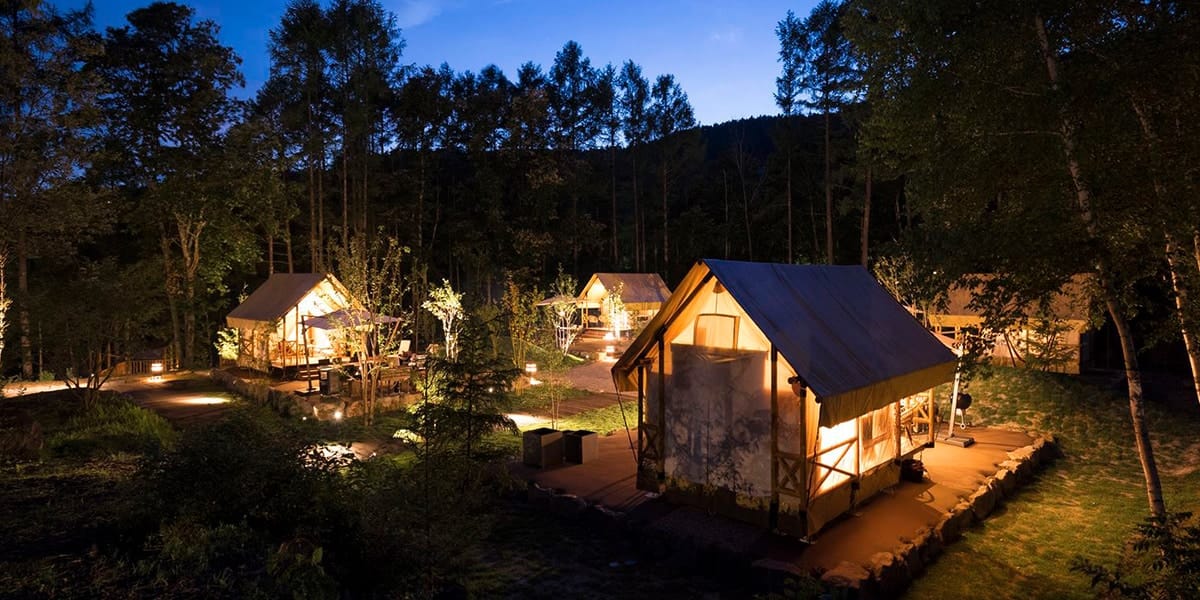 Illuminated glamping tents in a forest at Tateshina, highlighting a serene and rustic outdoor accommodation setting.