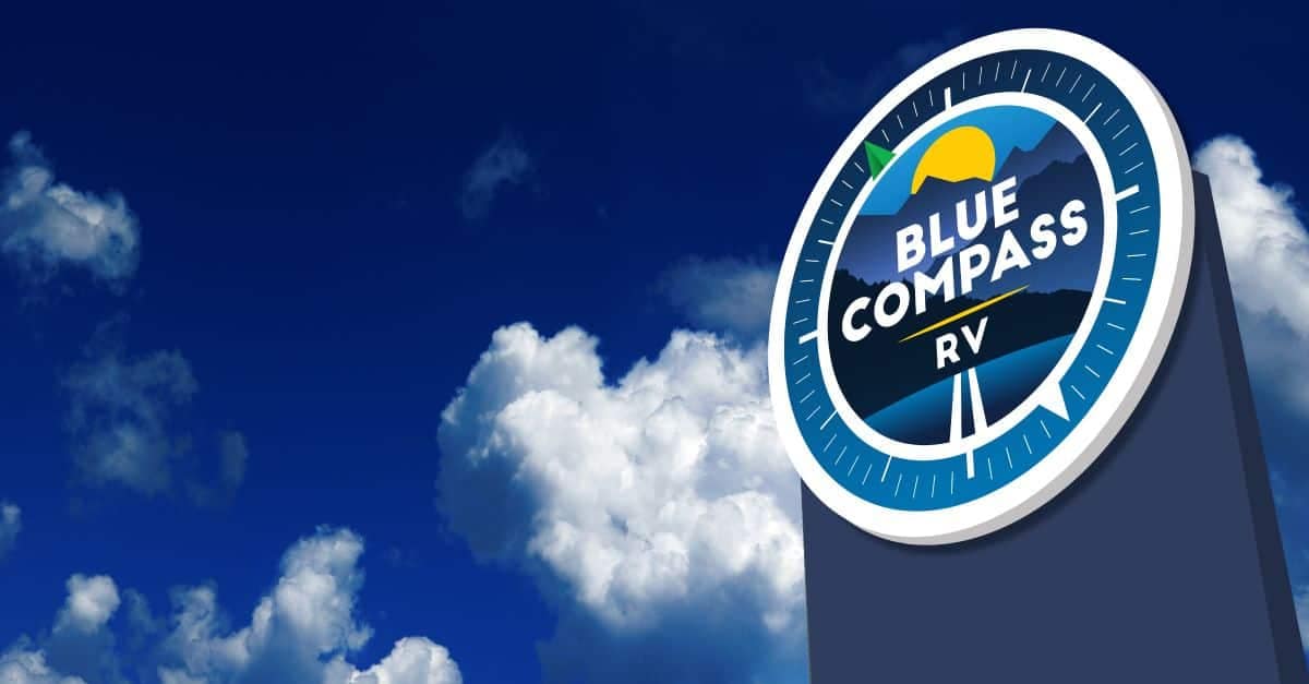 A Blue Compass RV sign in front of a cloudy sky.