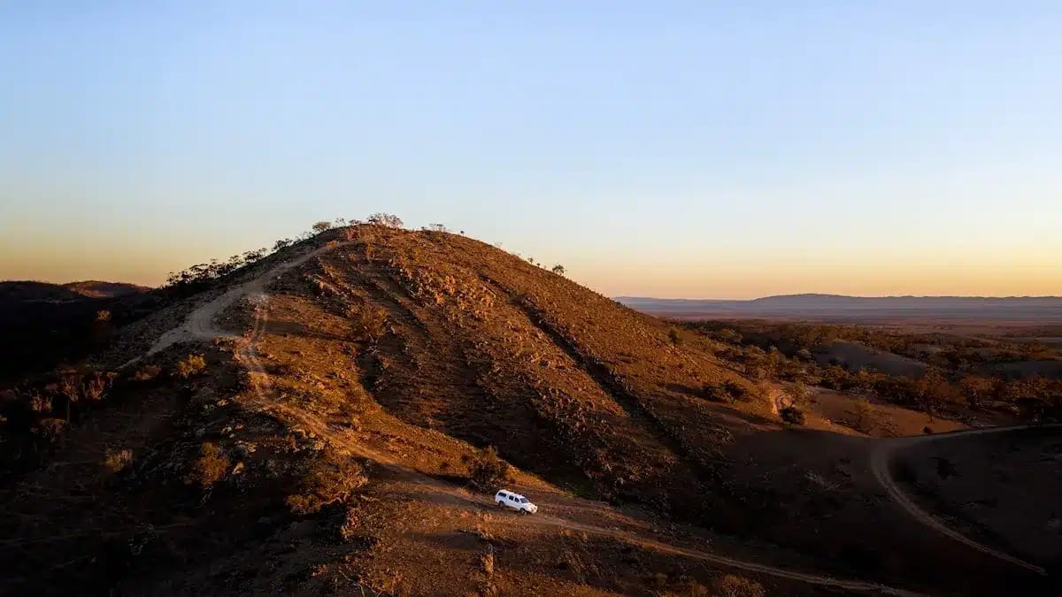 A vehicle driving on a winding dirt road along a ridge during sunset, auto-drafted to ensure precision.
