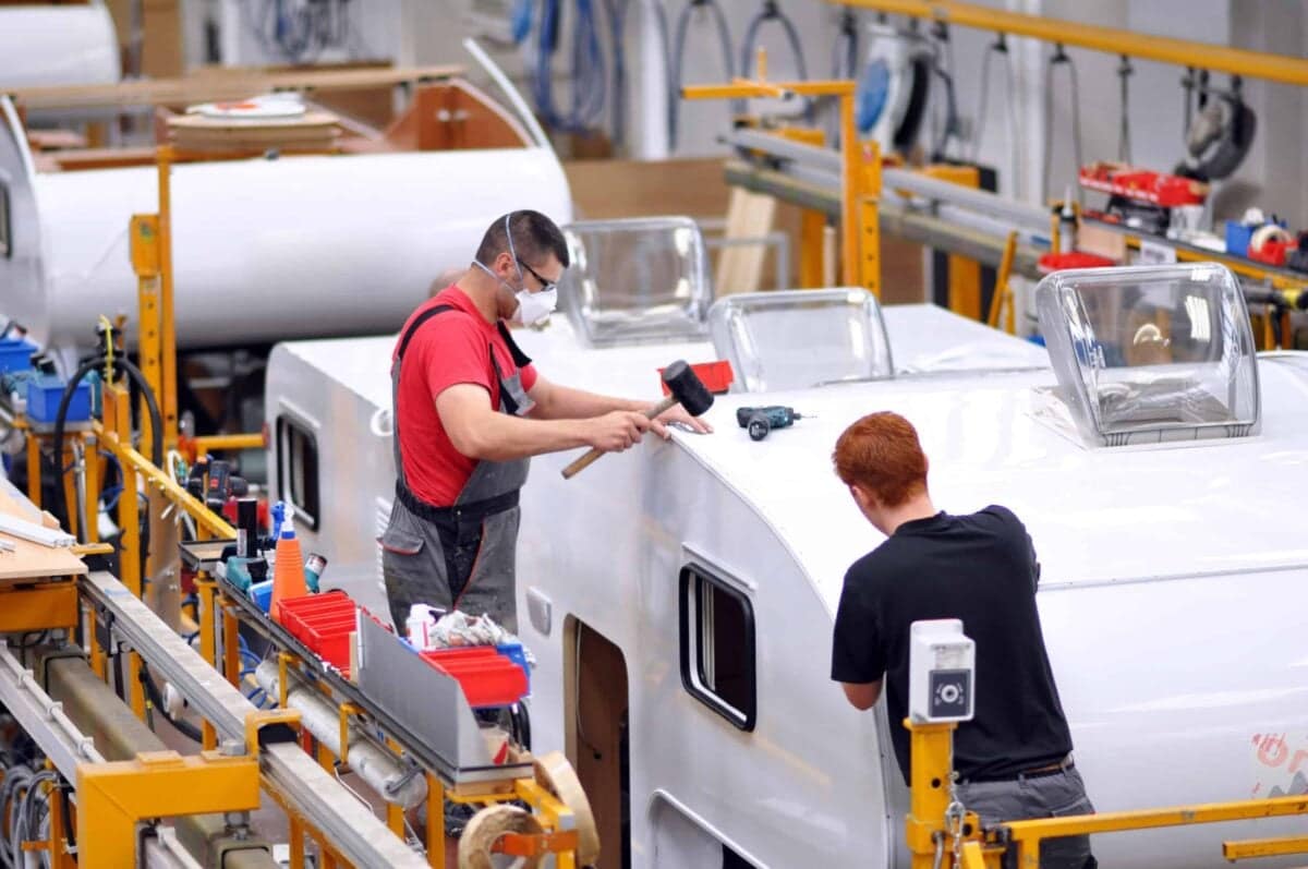 Two Australian men working on a white trailer in a factory.