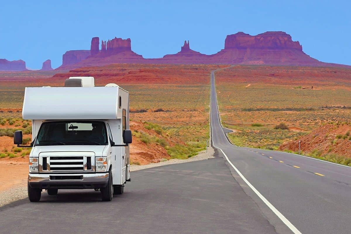A white RV driving down a desert road, highlighting the RV market.