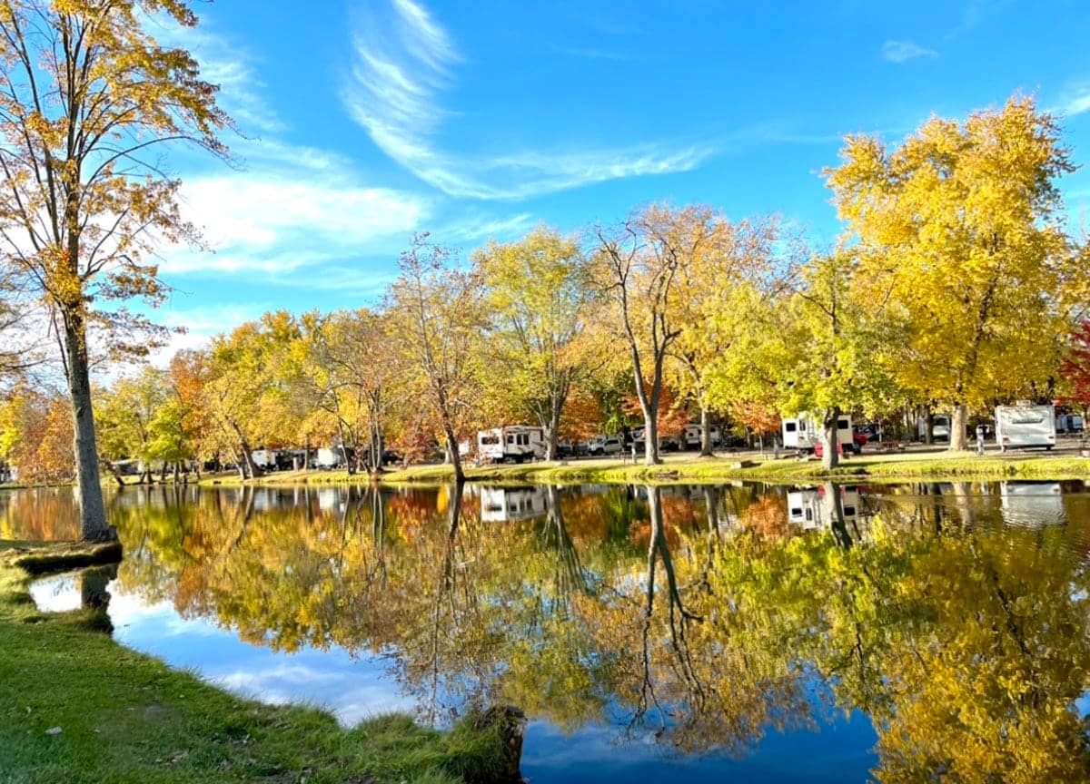Rv park on a lake with trees in the background, transforming into a Friendship Village campground.