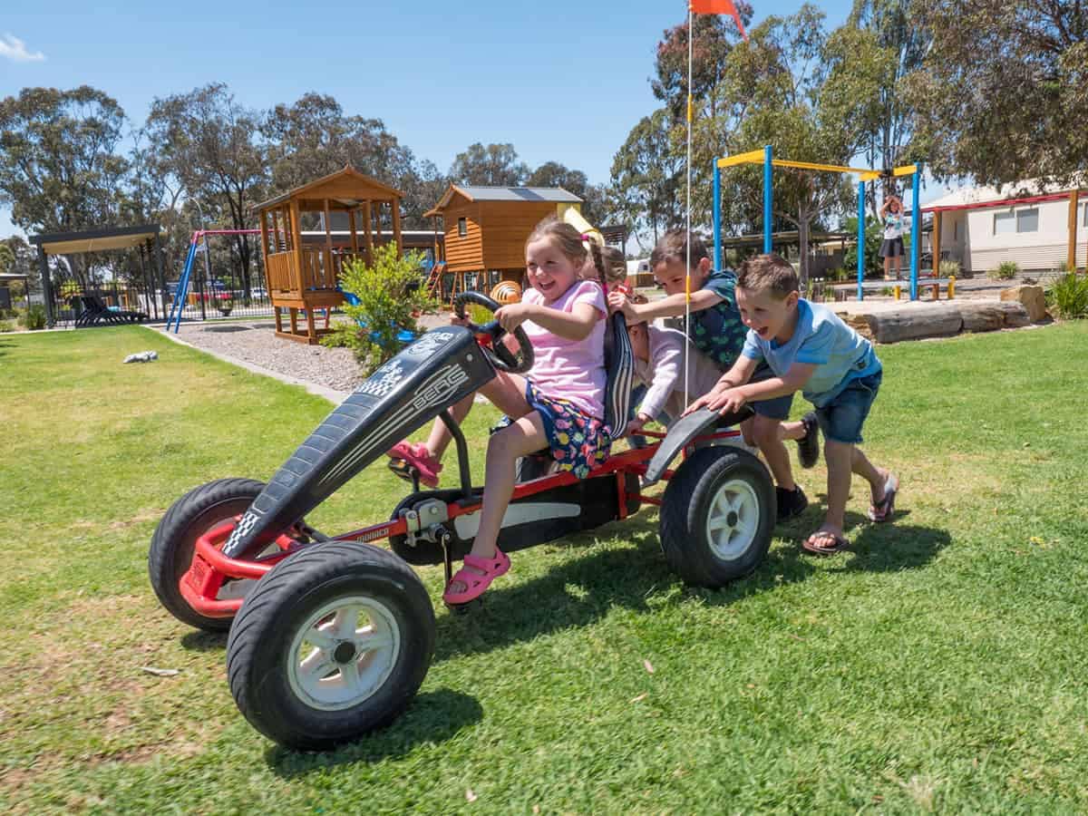 A group of children playing on a BIG4 toy car in a grassy area at Bendigo Marong Holiday Park.