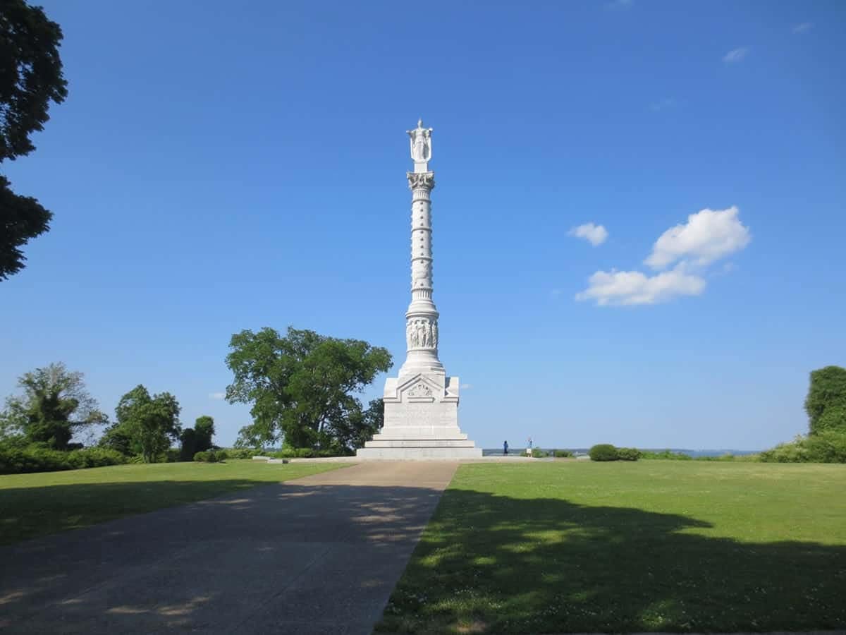 A white monument sits in the middle of Yorktown National Park, surrounded by a grassy field.