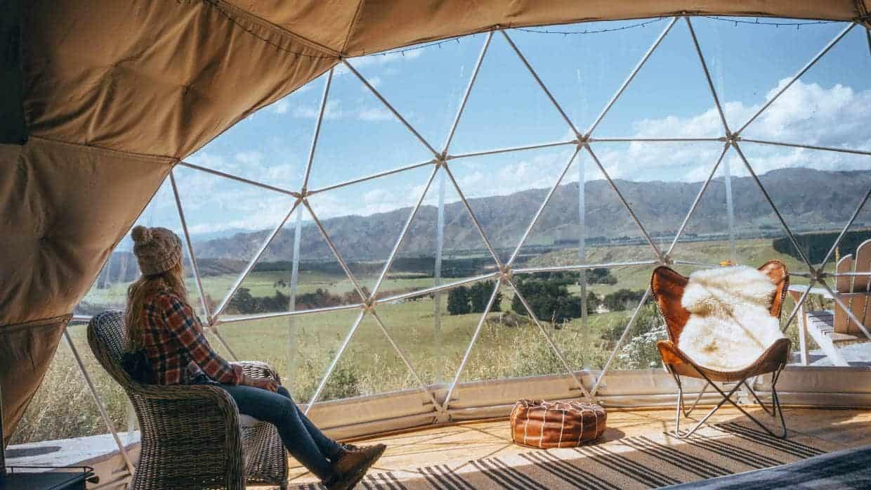 A woman enjoying a luxurious accommodation in a large dome while overlooking a picturesque field in New Zealand.