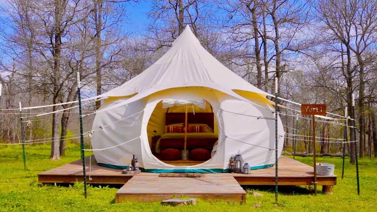 A white tent sits on a wooden deck in the woods, creating a tranquil retreat for nature enthusiasts.