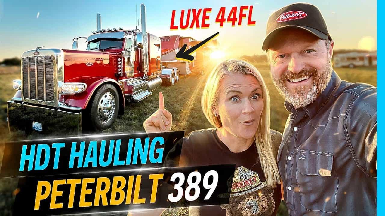 A man and woman standing next to a truck with the words ht hauling peterbilt 399 during a Luxe 44FL RV tour.