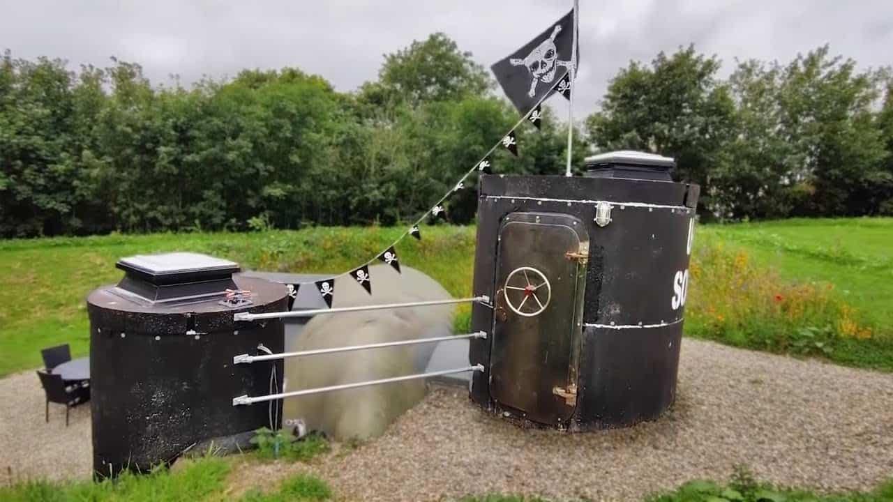 A large metal structure with a flag on it, resembling an HMS Sonar Glamping Pod.