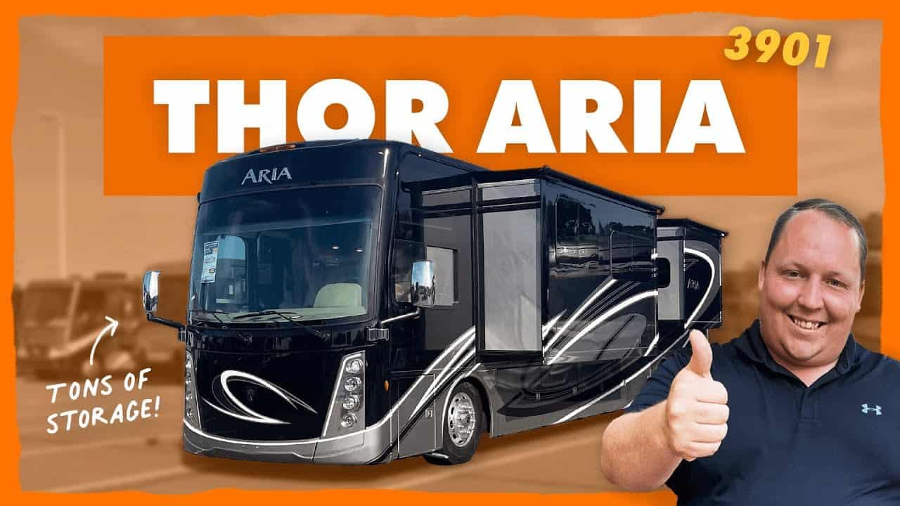 A man is giving a thumbs up in front of a Thor Aria, a Class A Diesel Pusher.
