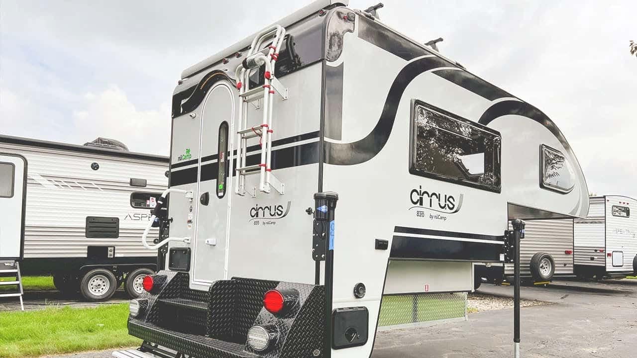 A 2022 nuCamp Cirrus 820, a black and white truck camper, parked in a parking lot.