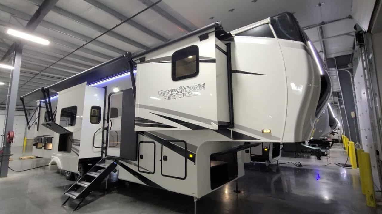 A white and black RV (2022 Riverstone Reserve 3950FWK) is parked in a warehouse, ready for an upcoming RV tour.