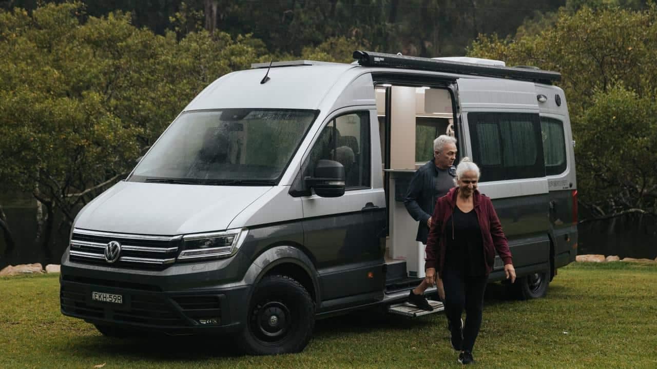 A couple standing next to a Volkswagen Kampervan.