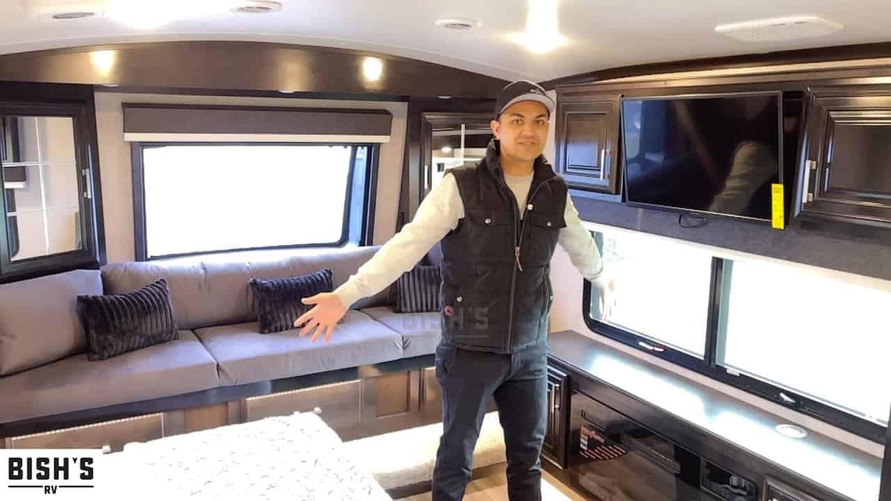 A man giving an RV tour of the 2022 Jayco Pinnacle 36 SSWS in the living room.