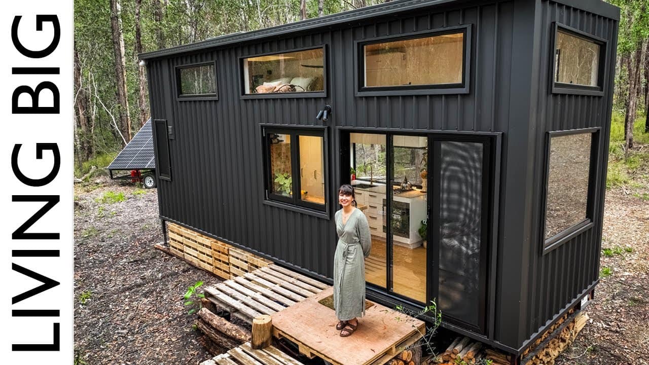 A woman is standing outside of a luxury tiny house in the woods, exuding simplicity.