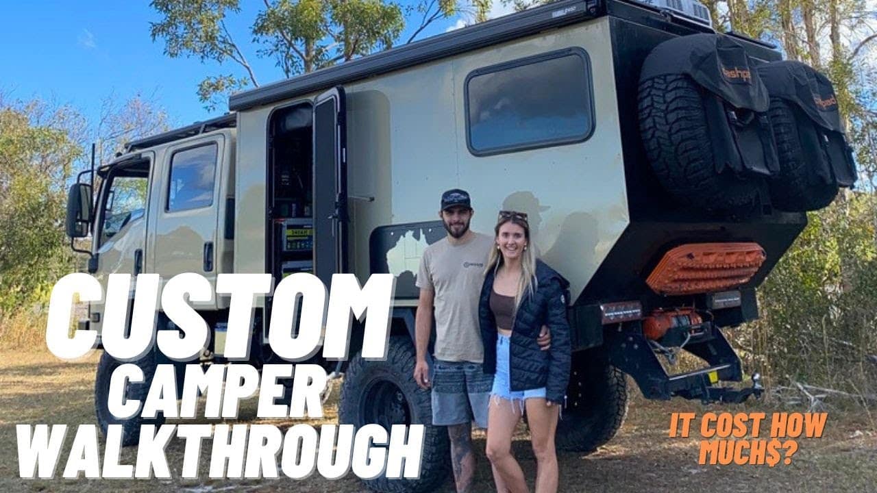 Two people standing next to an Isuzu NPS 300 truck with a custom camper walkthrough.