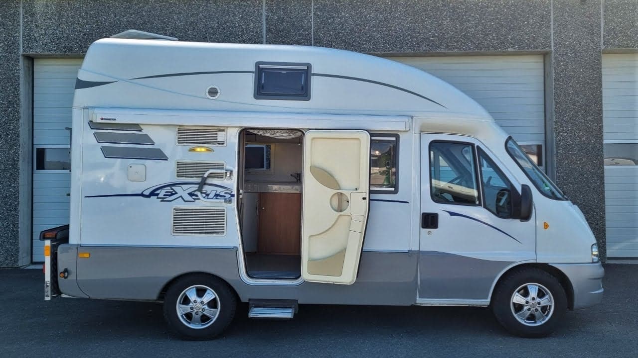 A compact camper van, the Hymer Exsis, parked in front of a garage.