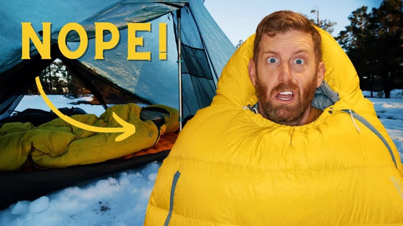 A man in a yellow sleeping bag experiencing a safe and enjoyable winter camping experience in front of a tent.