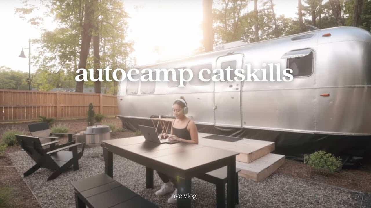 A woman is sitting at a table in front of an airstream trailer, which serves as her portable office for drafting.