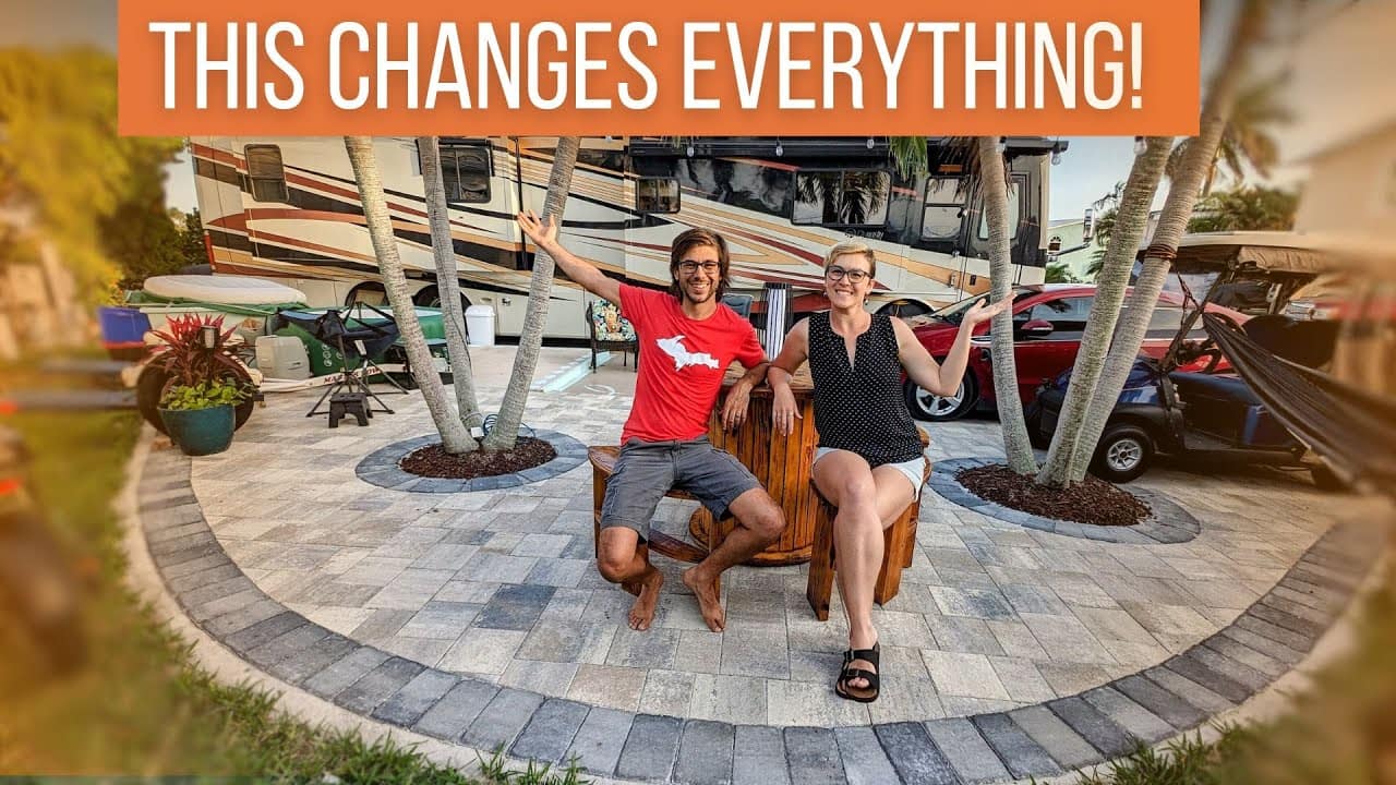 A couple celebrating outside their RV with arms raised in excitement, marking an auto draft.