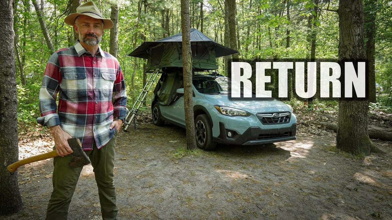 Man with an axe standing next to a car with a rooftop tent in the forest, with the words "Auto Draft" overlaid.