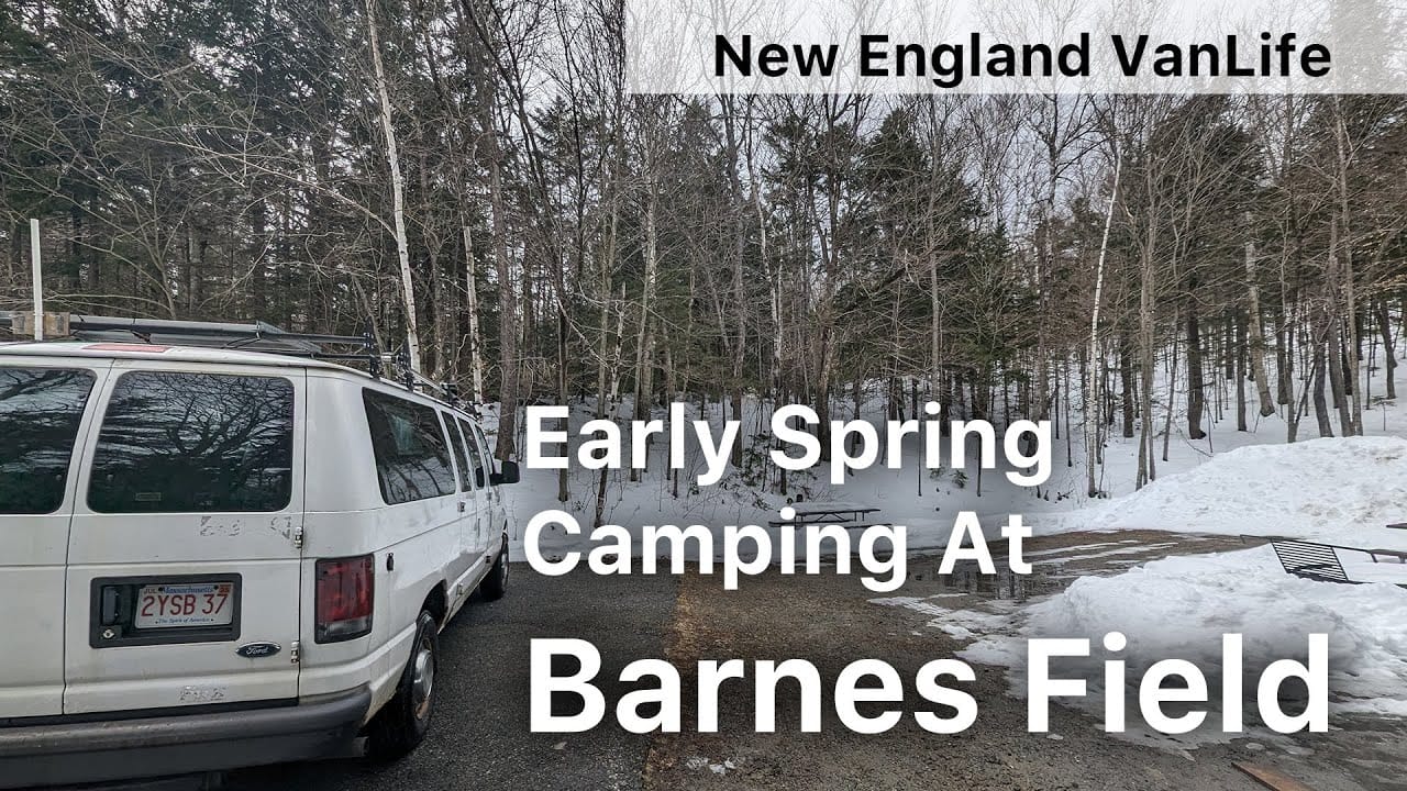 Two white vans parked on a gravel lot surrounded by leafless trees in a winter landscape, with text overlay "auto draft early spring camping at Barnes Field.