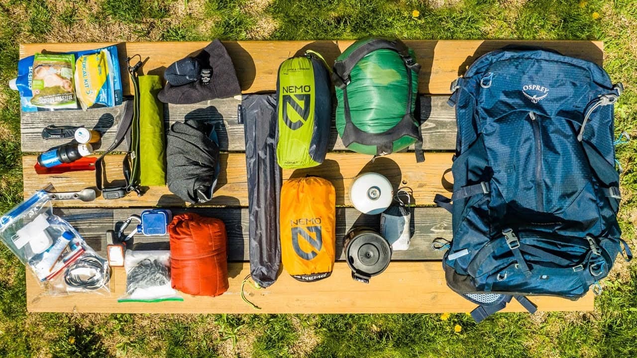 Various camping gear neatly arranged on a wooden table, ready for packing into a blue Auto Draft backpack.