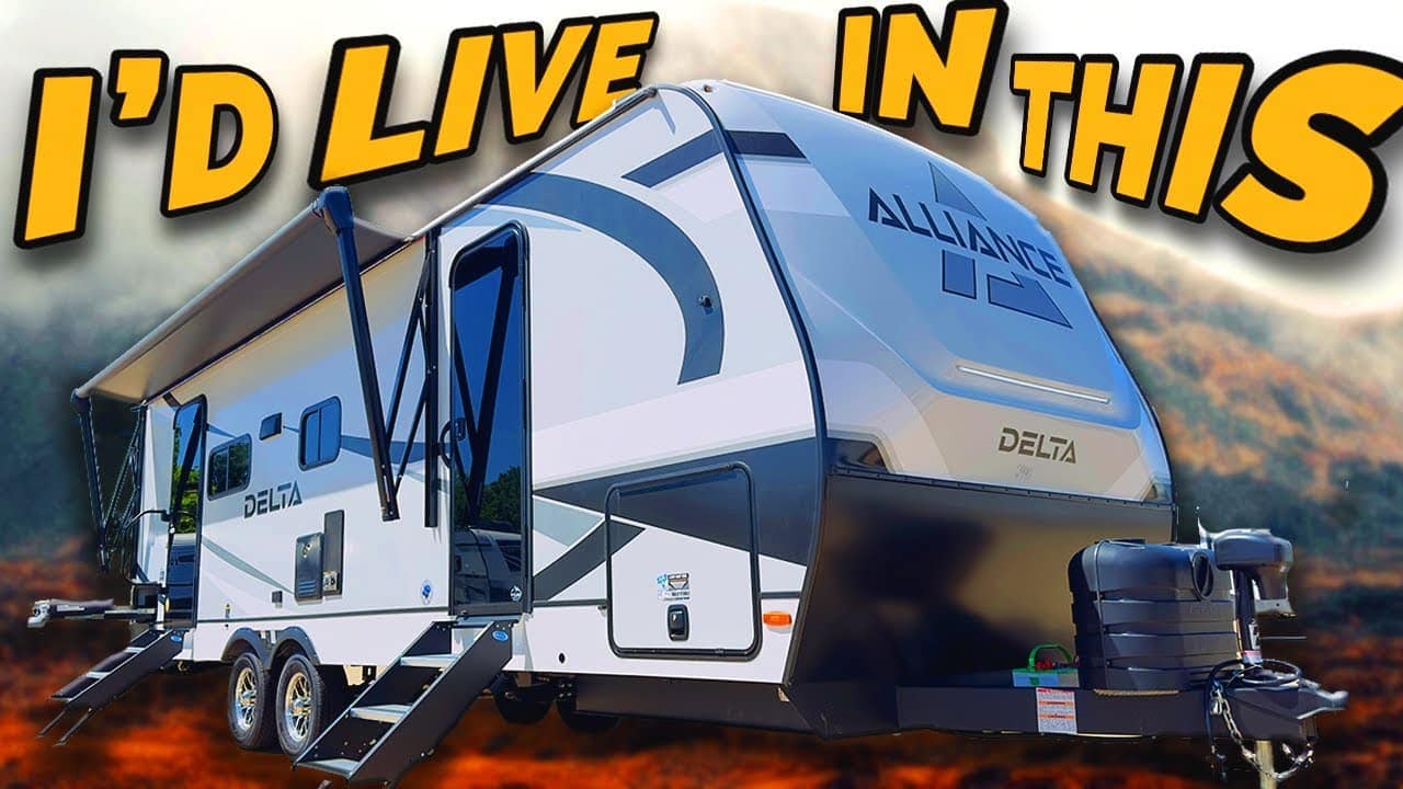 A modern rv with expanded sections parked outdoors, featuring bold text "i'd live in this" above, set against a misty forest backdrop.