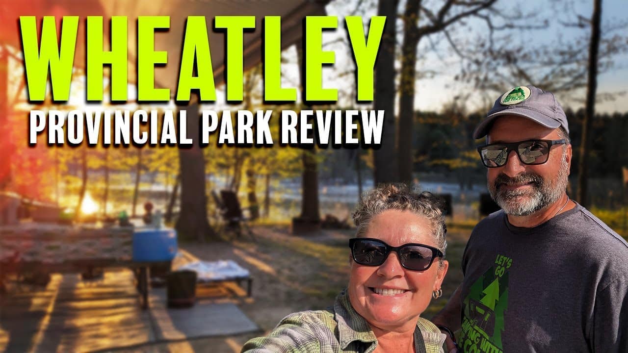 A couple smiles at the camera with a sunset background at Wheatley Provincial Park; auto draft overlay reads "WHEATLEY PROVINCIAL PARK REVIEW.