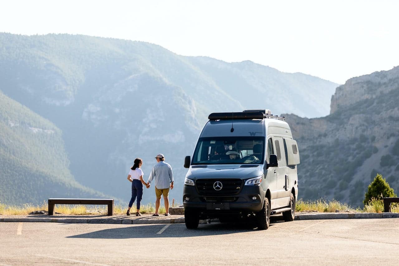 Two people standing outdoors in front of a camper van with mountains in the background, showcasing the Outdoorsy experience offered by Lead Bank's RV loan product.