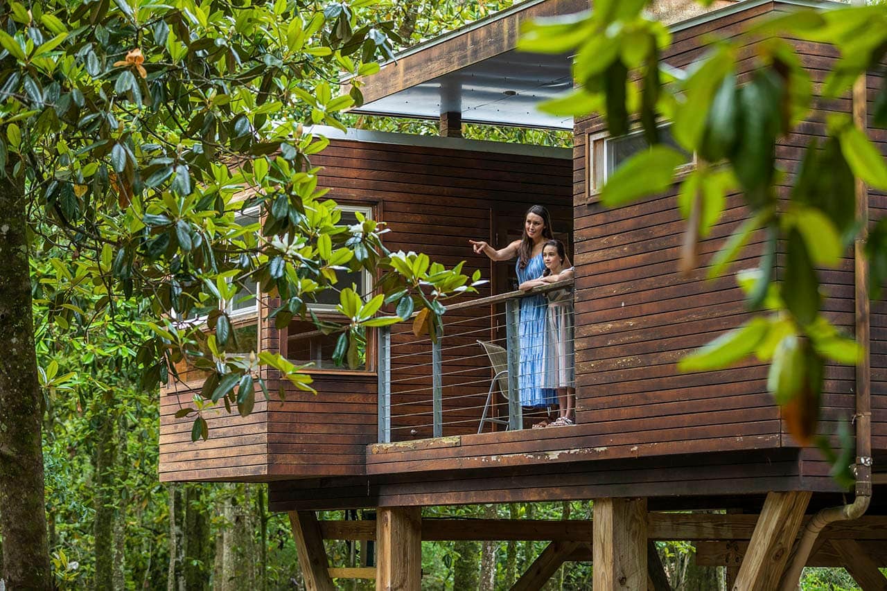 A woman is standing on the balcony of a tiny house nestled in Coldwater Gardens.