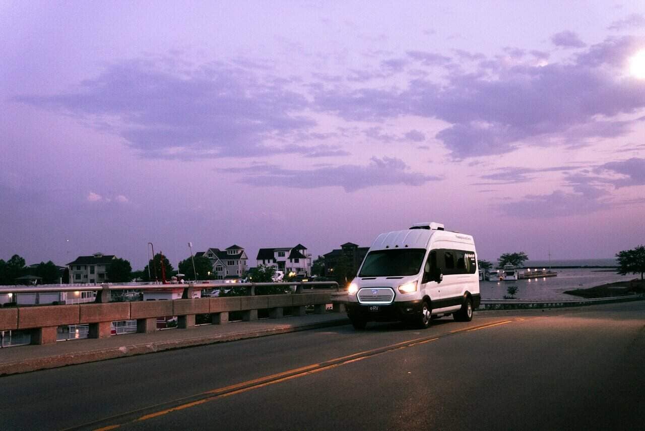 A white van driving on a bridge at dusk.