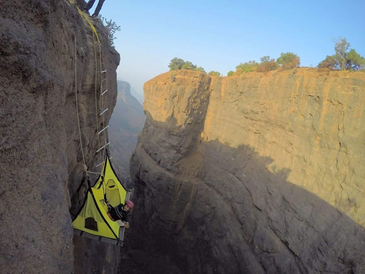 A man is cliff camping in the Sandhan Valley wilderness, hanging from a rope on the side of a cliff.