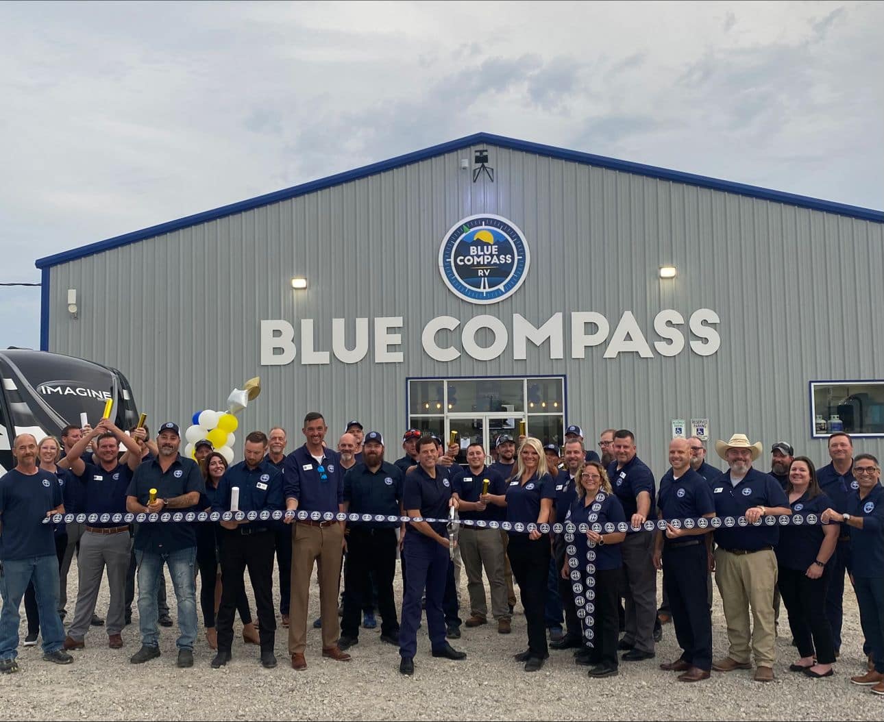 A group of people standing in front of a Brand building, featuring the iconic Blue Compass RV design.
