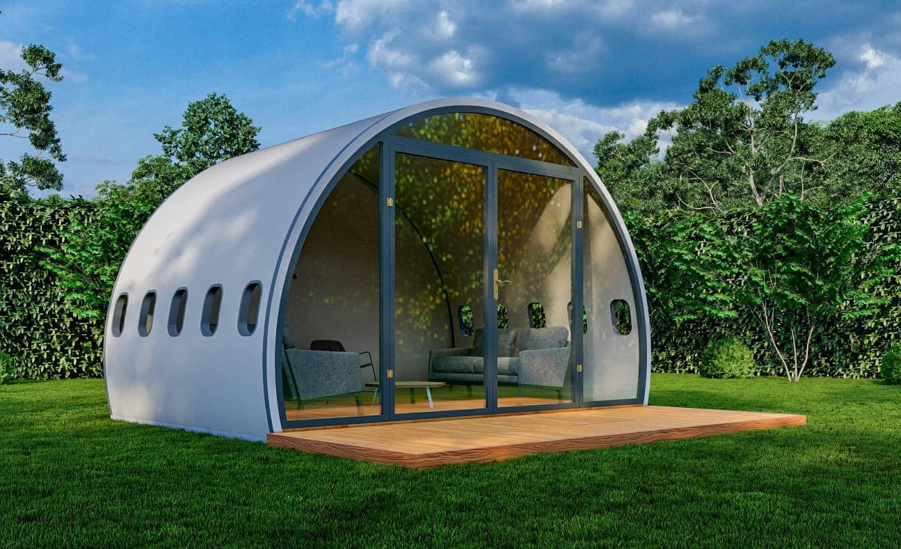 An upcycled airplane-shaped house nestled in a grassy area.